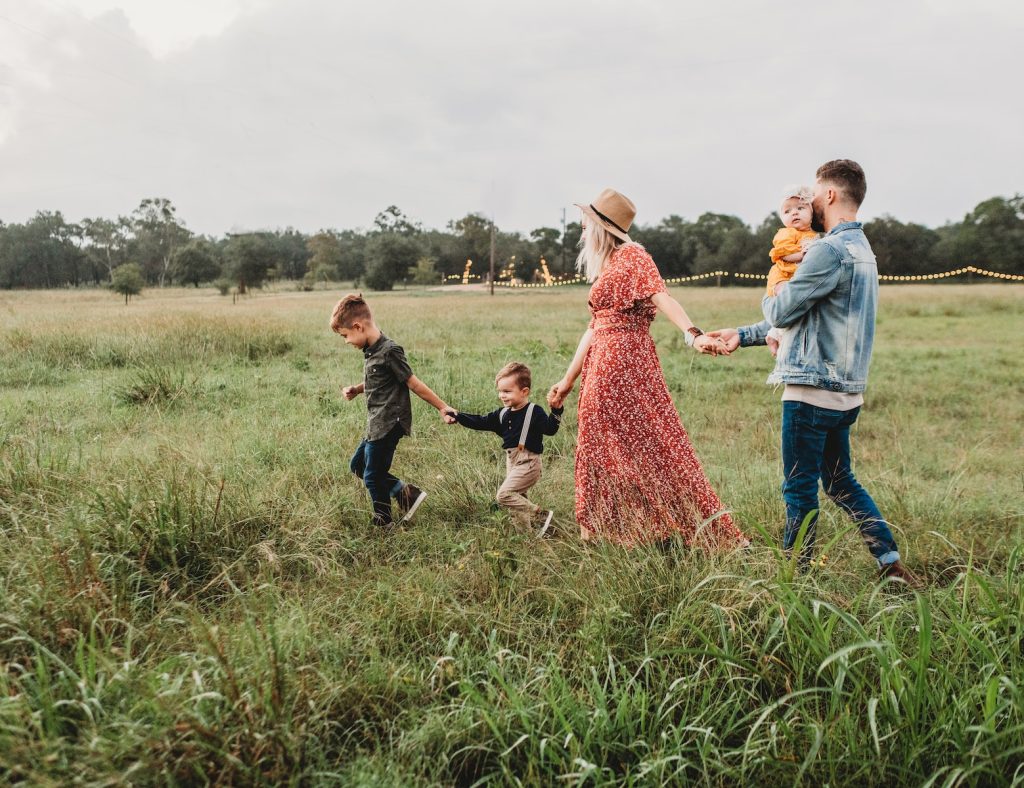 Une famille se promène dans un champ herbeux en se tenant la main.