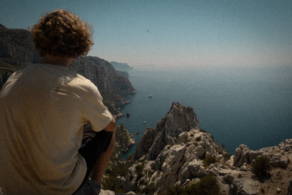 man sitting on rocky cliff facing ocean