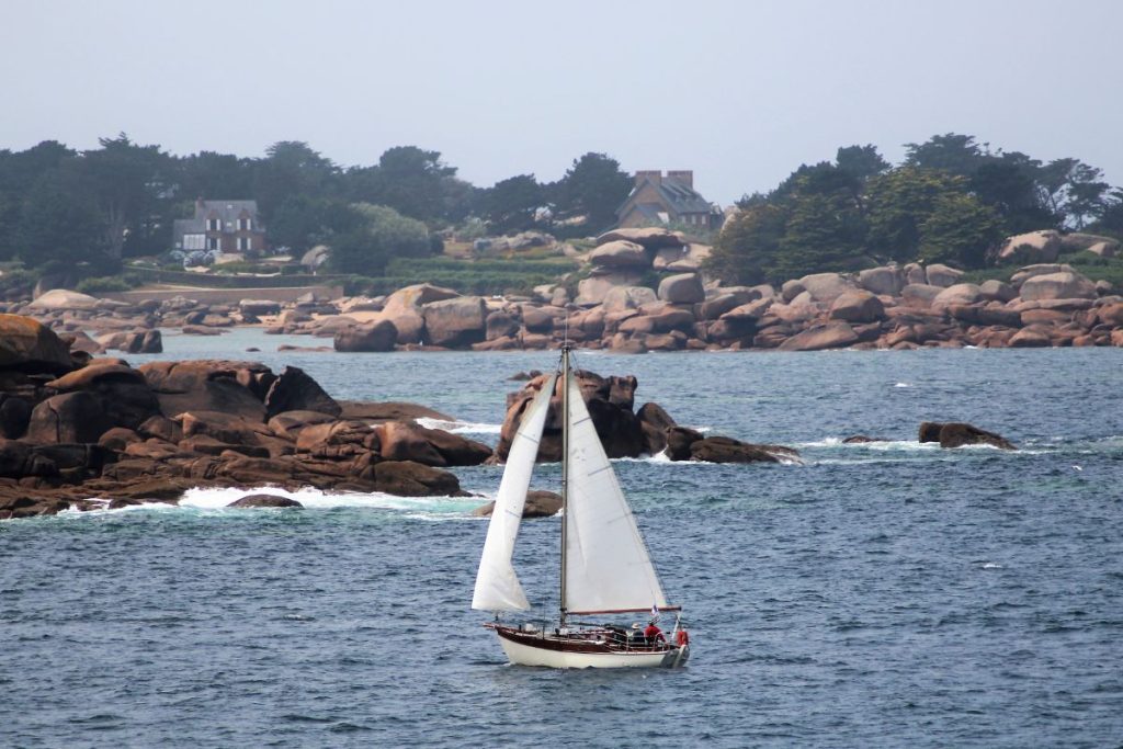 Un voilier navigue dans l'océan près de quelques rochers.
