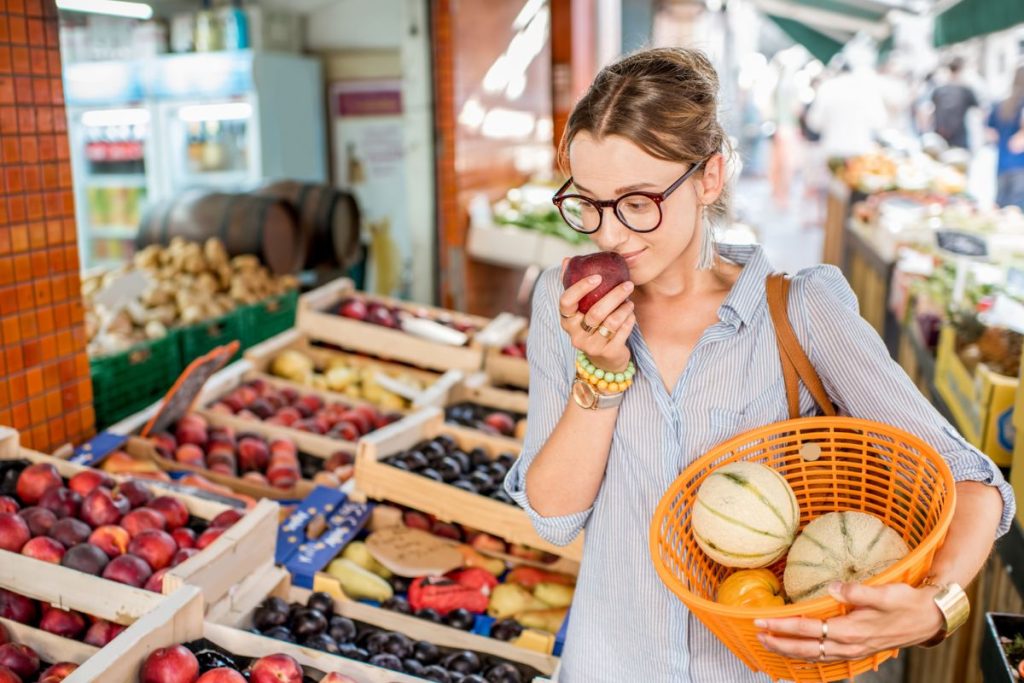 Une femme tient une corbeille de fruits devant un marché.