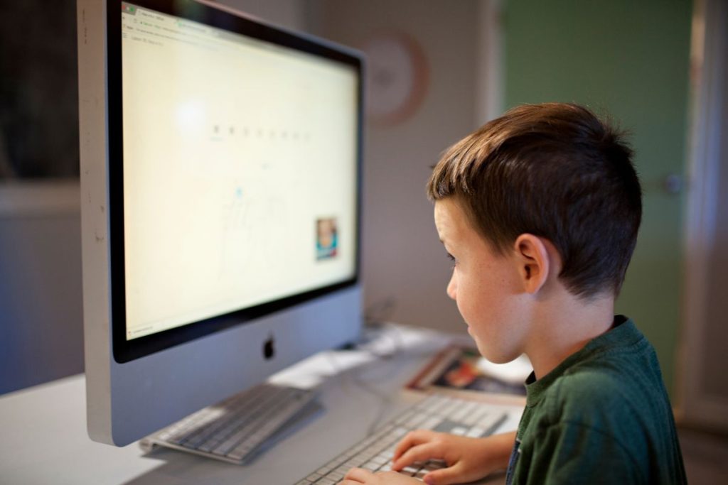 Un jeune garçon assis devant un écran d’ordinateur.