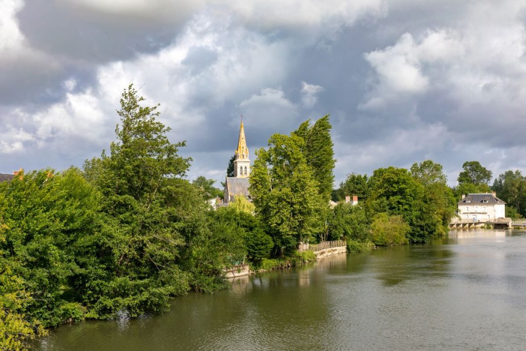 Une rivière avec des arbres et une église en arrière-plan.