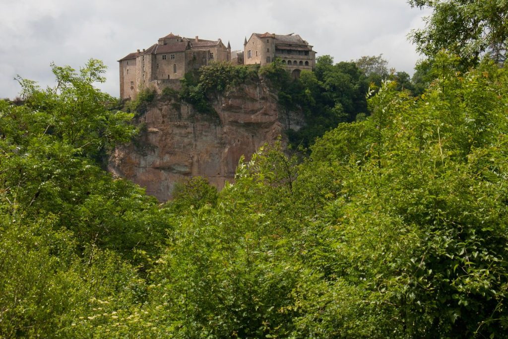 Un château se dresse au sommet d’une falaise entouré d’arbres.