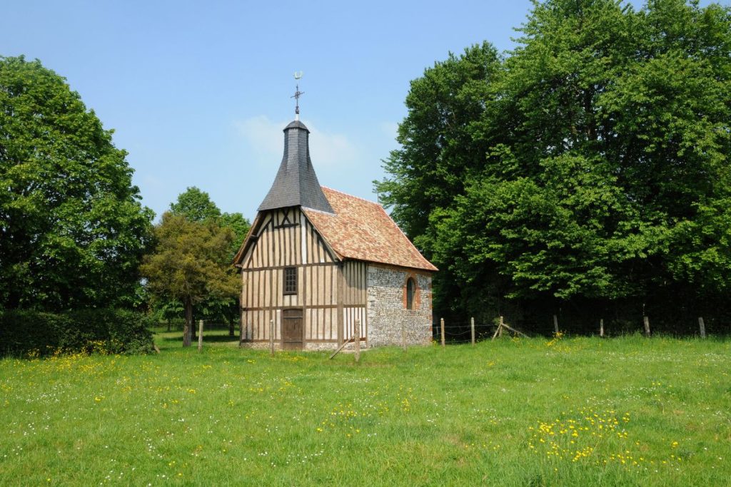 Une petite église en bois dans un champ herbeux.