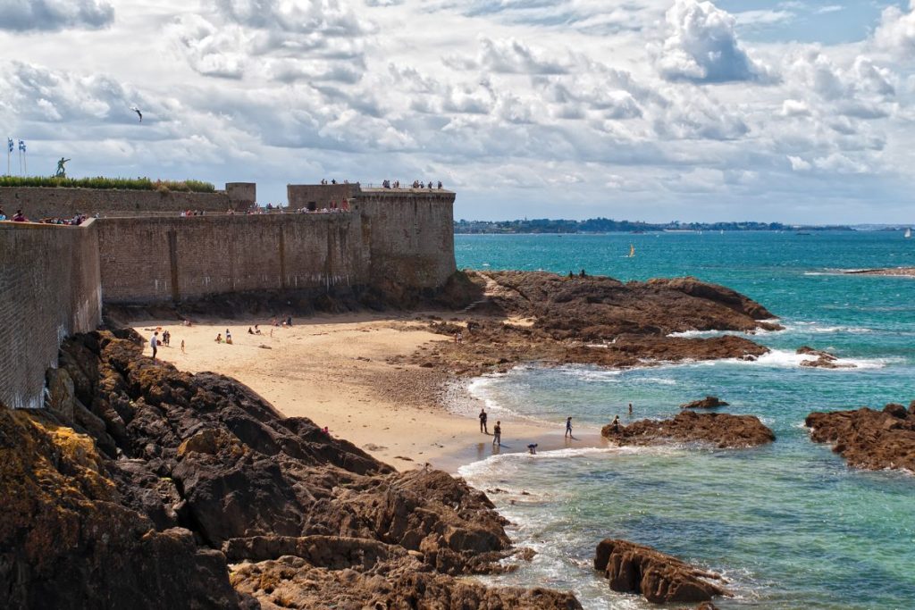 Un château se dresse sur une falaise rocheuse surplombant une plage.