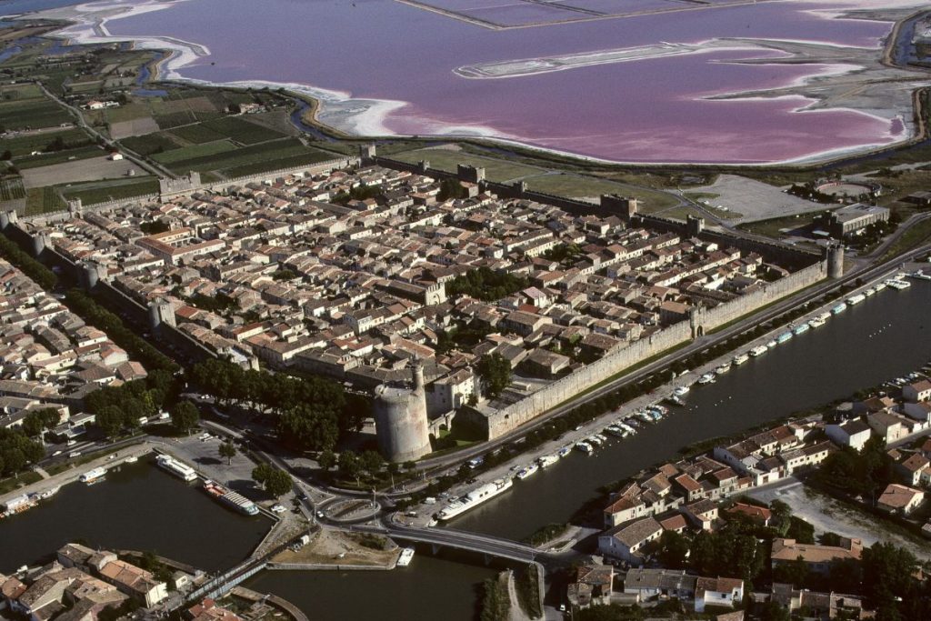 Vue aérienne d'une ville fortifiée avec canaux et lac salé rose en arrière-plan.