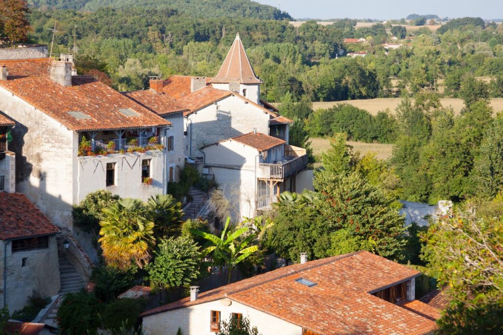 Vue sur les toits d'un village européen avec des maisons blanches traditionnelles et un clocher d'église entouré d'une verdure luxuriante.
