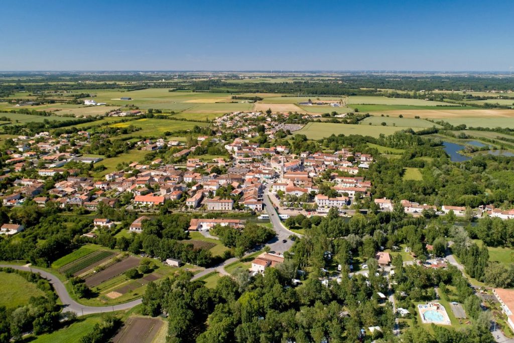 Vue aérienne d'un village pittoresque entouré de champs et de verdure par temps clair.