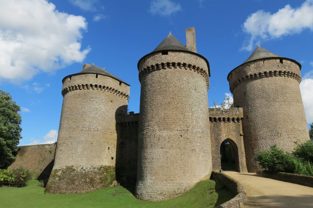 Une forteresse médiévale avec des tours cylindriques sous un ciel bleu.