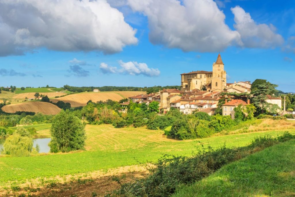 Un paysage rural pittoresque avec une église historique s'élevant au-dessus d'un petit village entouré de champs vallonnés sous un ciel bleu avec des nuages épars.