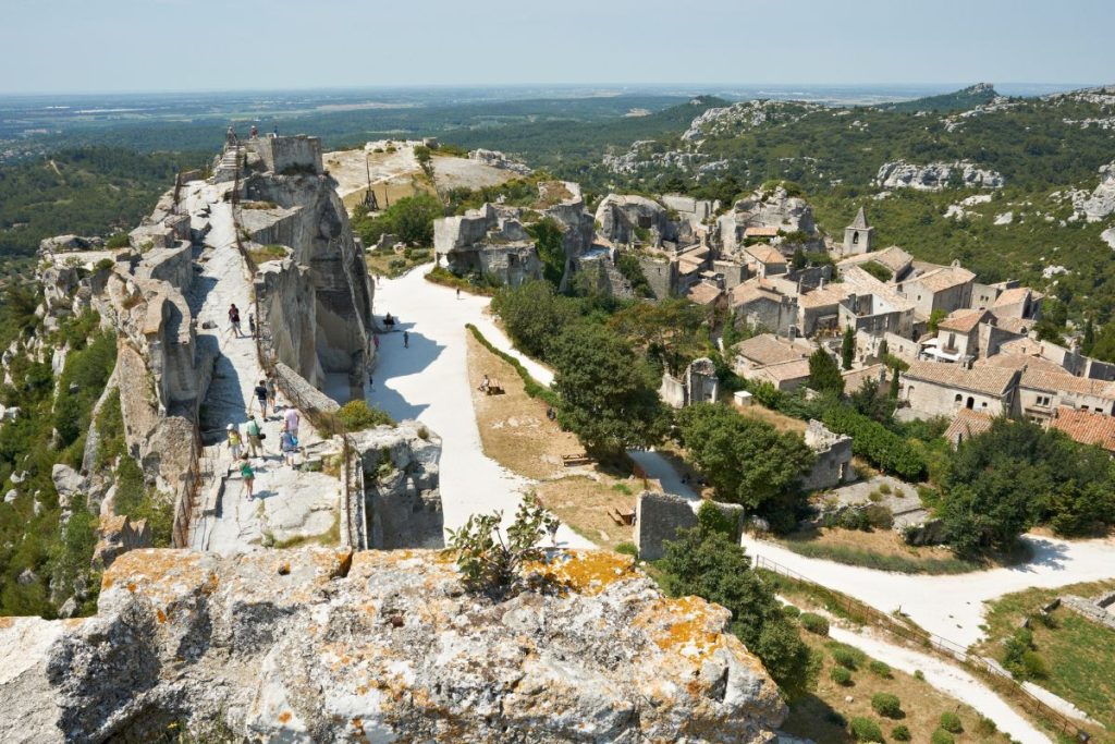 Vue aérienne d'un village historique niché sur une falaise rocheuse avec des visiteurs explorant le paysage pittoresque.