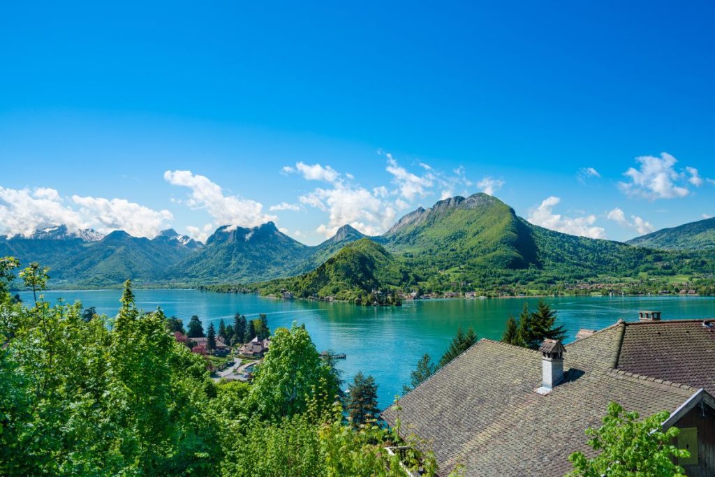 Vue panoramique sur un lac tranquille avec les montagnes environnantes et la verdure sous un ciel bleu clair.