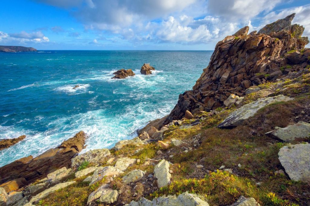 Falaises côtières rocheuses contre un océan bleu vif avec des calottes blanches sous un ciel partiellement nuageux.