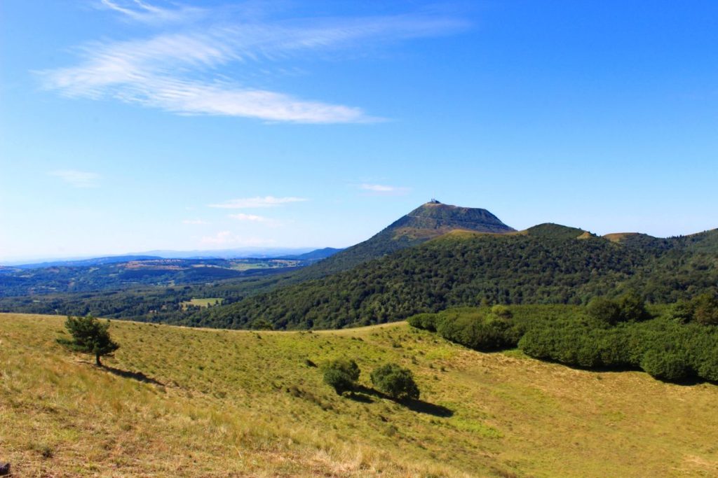 Une vue panoramique sur une colline verdoyante menant à un sommet de montagne important sous un ciel bleu avec des nuages vaporeux.