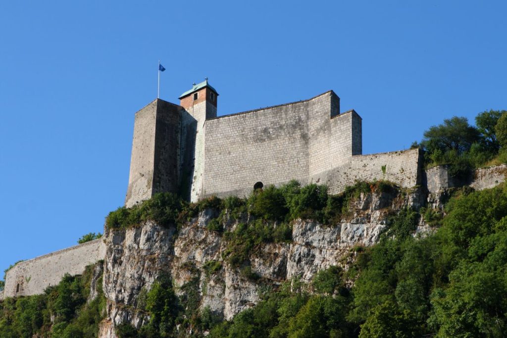 Une forteresse de pierre perchée au sommet d’une falaise abrupte sous un ciel bleu clair.