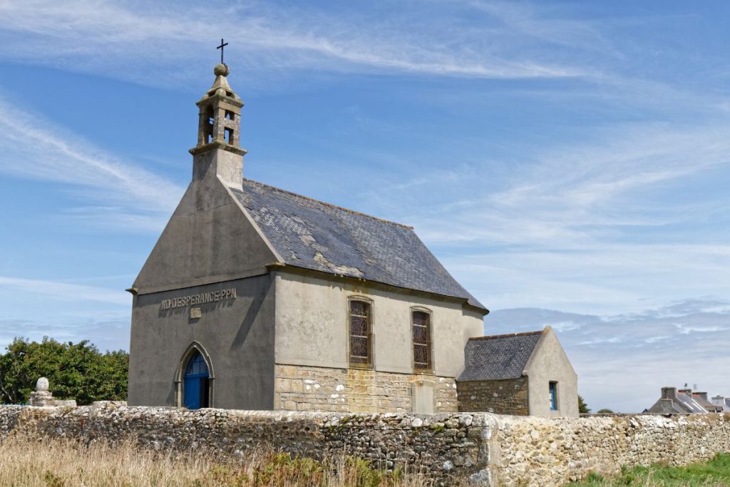 Charmante ancienne chapelle en pierre avec une porte bleue sous un ciel dégagé.