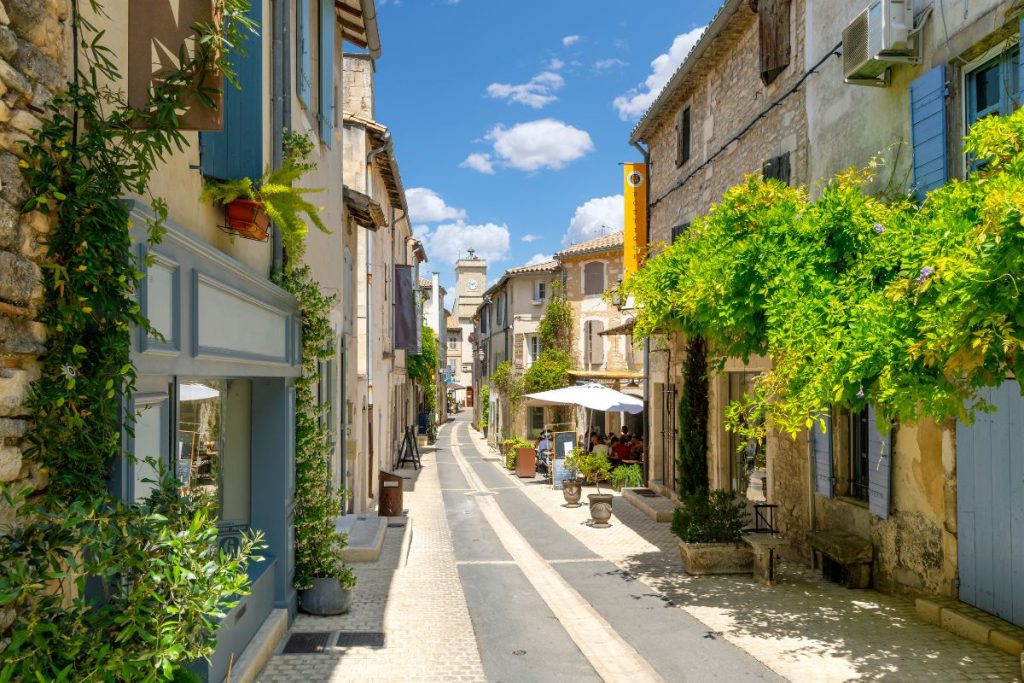 Rue pavée pittoresque bordée de maisons traditionnelles et de verdure sous un ciel bleu clair dans un village européen.