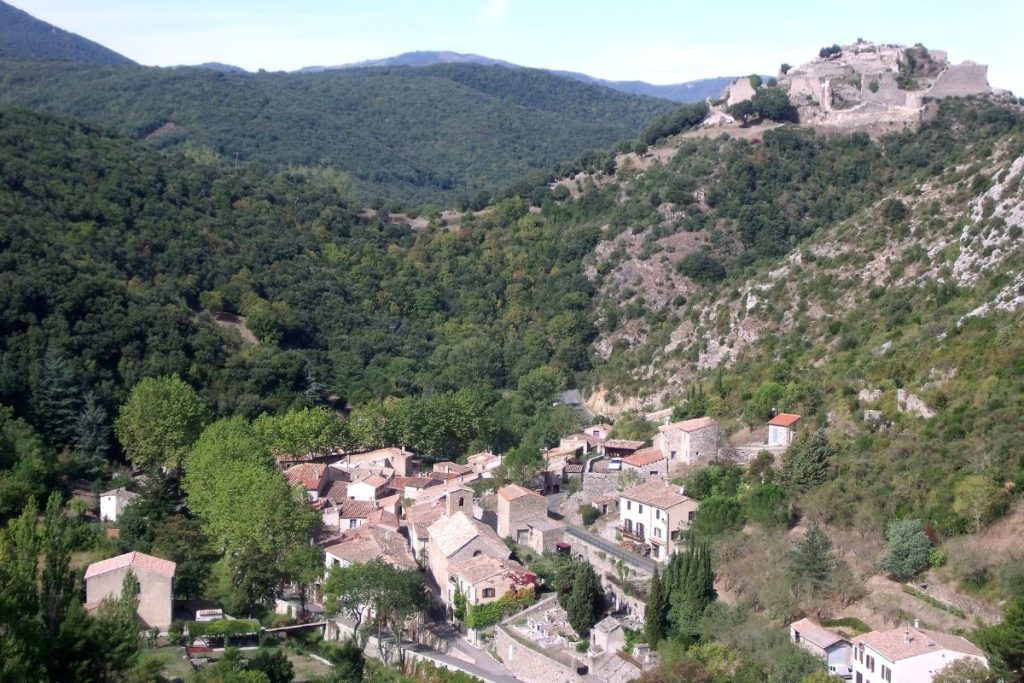 Une vue panoramique sur un village traditionnel niché dans un écrin de verdure avec en arrière-plan une forteresse sur une colline.