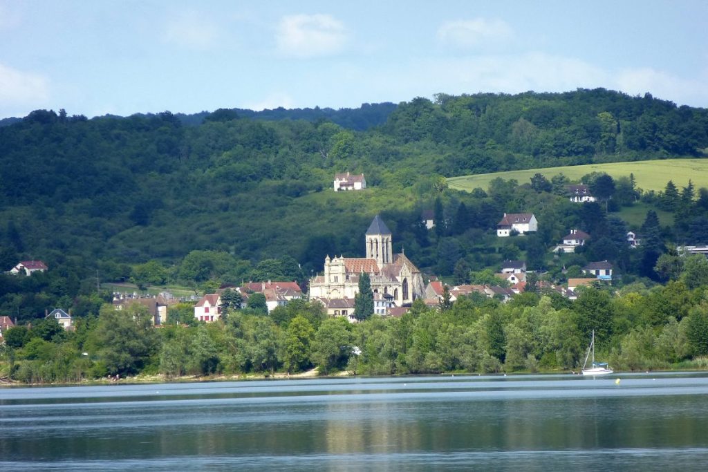 Une vue panoramique sur un village européen au bord de l'eau avec des collines verdoyantes en arrière-plan.