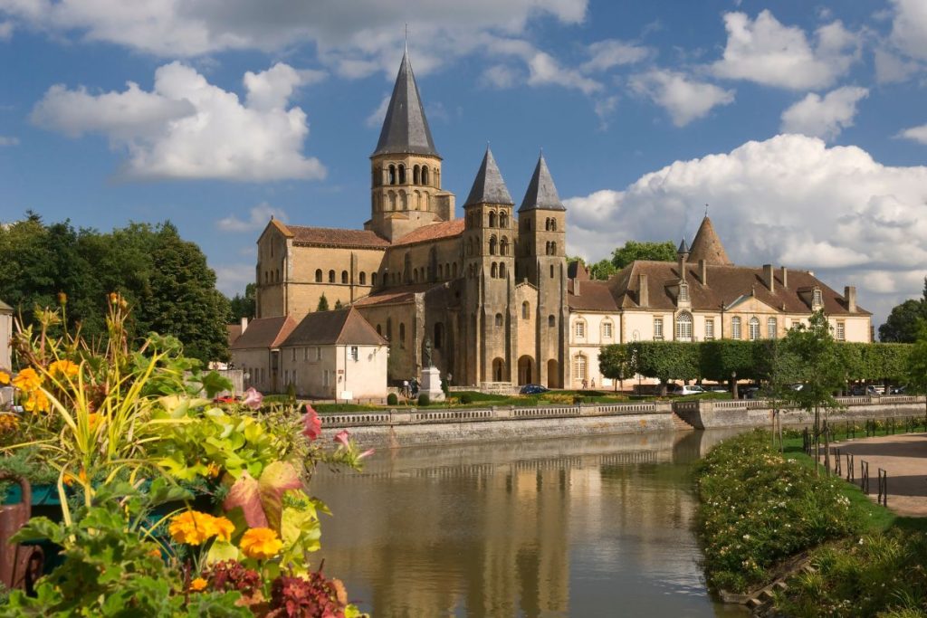 Abbaye médiévale au bord d'une rivière avec des fleurs colorées au premier plan par une journée ensoleillée.