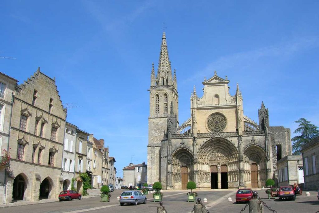 Cathédrale historique avec des flèches flanquées de bâtiments sous un ciel bleu clair.