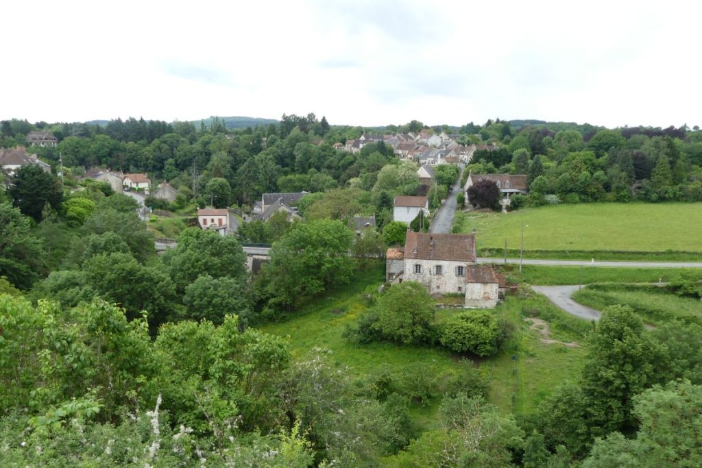 Vue aérienne d'un village pittoresque avec des bâtiments traditionnels en pierre, entourés d'une verdure luxuriante et d'arbres.