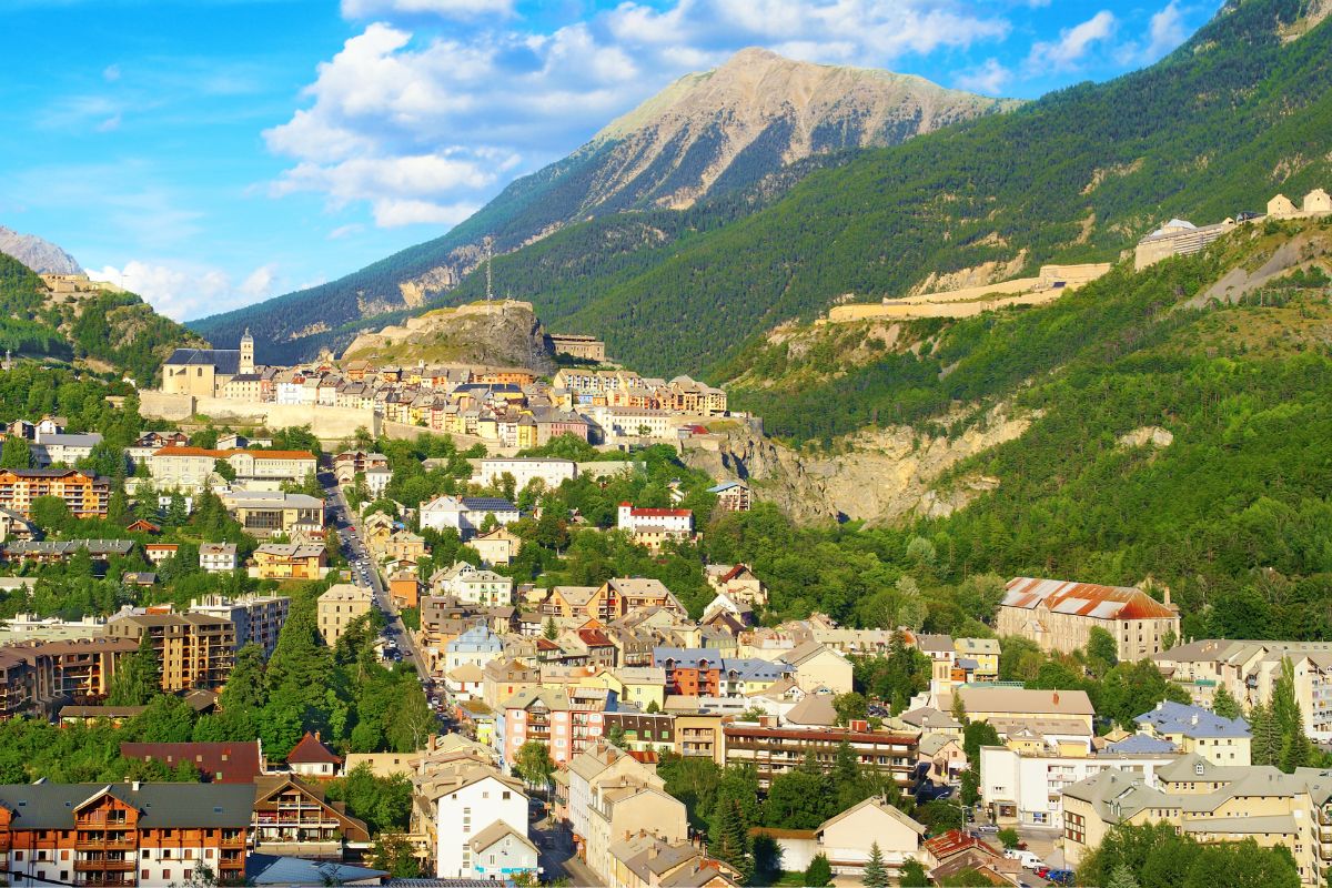 Vue panoramique d'une ville de montagne avec des bâtiments colorés, nichée sous de grandes collines et un ciel bleu clair.