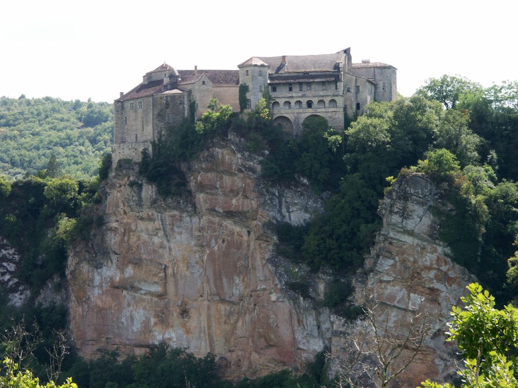 Une ancienne forteresse en pierre perchée au sommet d’une falaise abrupte entourée d’un feuillage vert luxuriant.