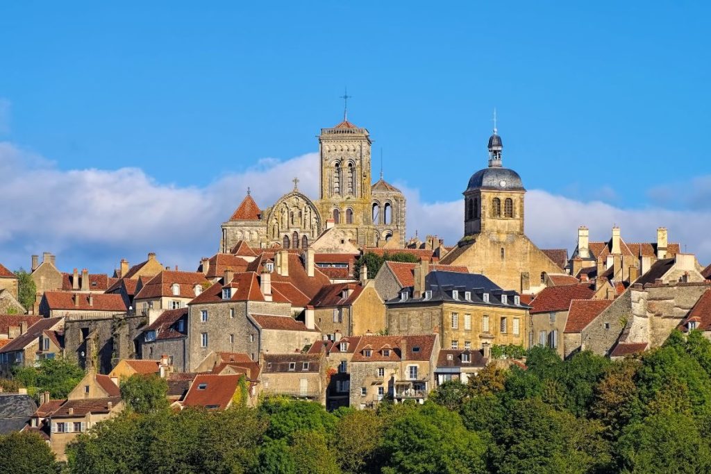 Une vue pittoresque sur un village historique avec des bâtiments traditionnels en pierre et des clochers proéminents sur un ciel bleu clair.