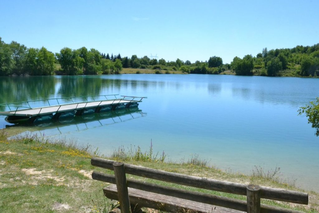 Lac paisible avec une rangée de canoës amarrés sur une jetée, entouré d'une végétation luxuriante et d'un ciel bleu clair. une clôture en bois est visible au premier plan.
