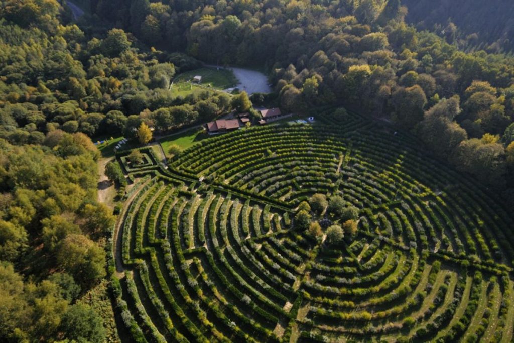 Vue aérienne d'un jardin disposé symétriquement aux motifs circulaires, entouré d'arbres et d'une maison à la campagne.