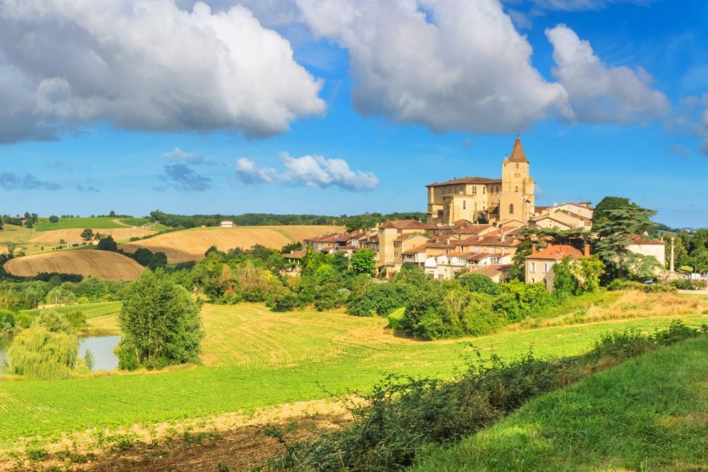 Un village pittoresque avec une église en pierre proéminente, niché au milieu de collines verdoyantes sous un ciel bleu clair.