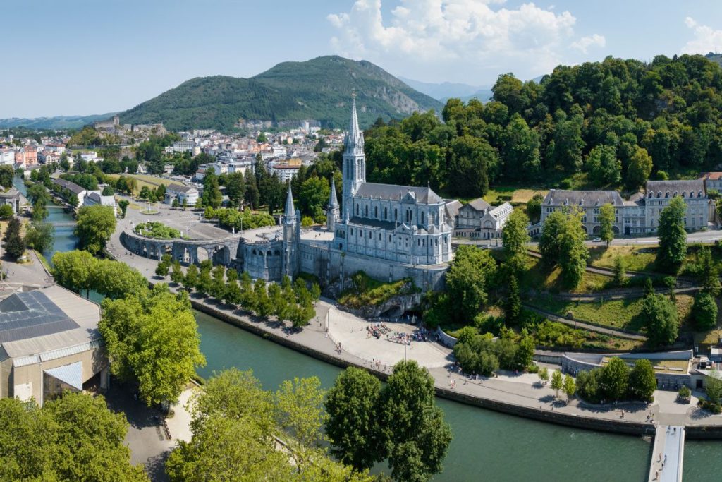 Vue aérienne d'une ville européenne historique avec une cathédrale importante au bord de la rivière, entourée d'une verdure luxuriante et de collines.