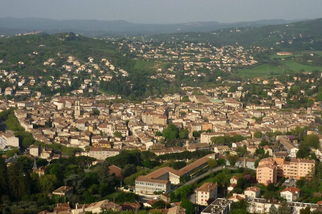 Vue aérienne d'une ville densément peuplée avec des bâtiments serrés, entourée de collines verdoyantes.