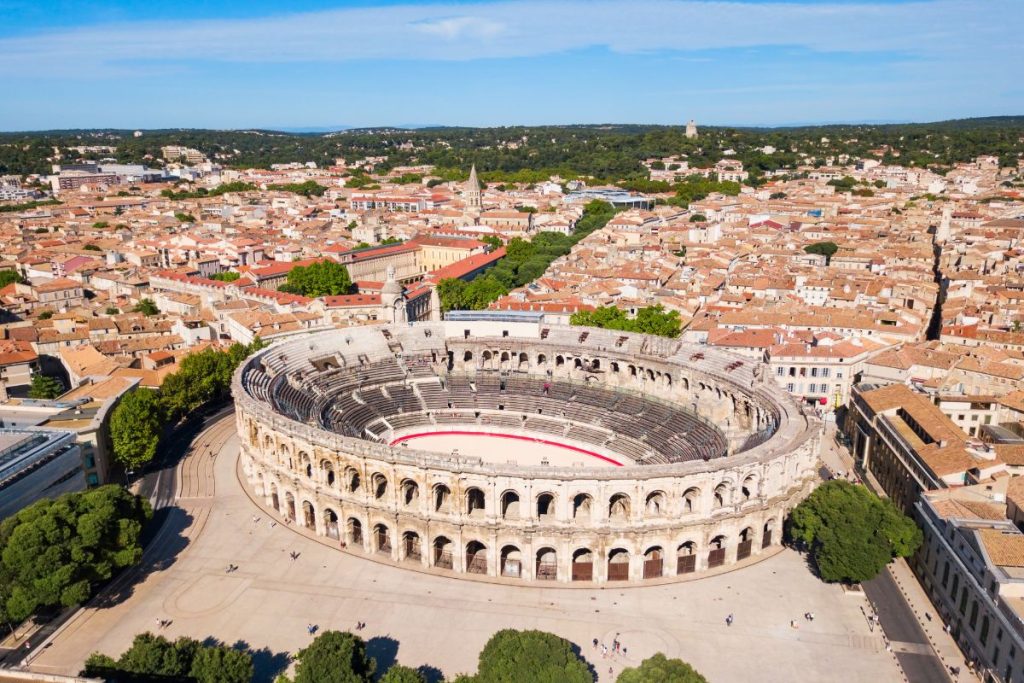 Vue aérienne de l'ancien amphithéâtre romain de Nîmes, en France, montrant la structure ovale bien conservée entourée par le paysage urbain par temps clair.