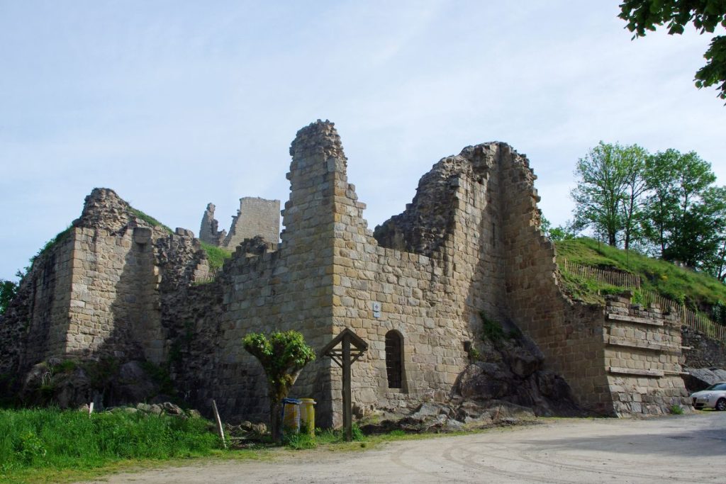 Ruines d'un château médiéval en pierre par une journée ensoleillée avec de la verdure en arrière-plan.