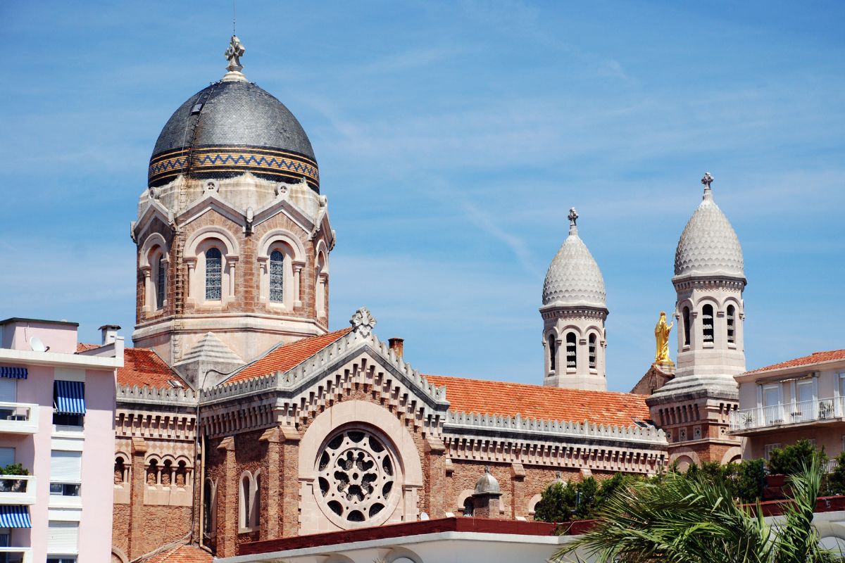 Église historique à l'architecture richement ornée, comprenant un vitrail circulaire et des tours jumelles en forme de dôme sur un ciel bleu clair.