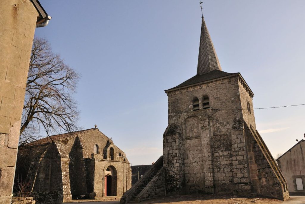 Église en pierre avec flèche dans un cadre champêtre sous un ciel clair.