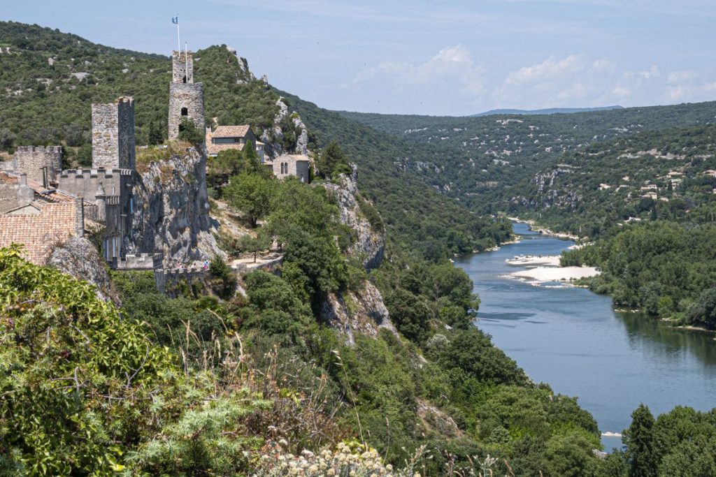 Des bâtiments en pierre et une tour sur une falaise surplombent une rivière sinueuse entourée de verdure luxuriante et de collines. Des bâtiments en pierre et une tour sur une falaise surplombent une rivière sinueuse entourée de verdure luxuriante et de collines.