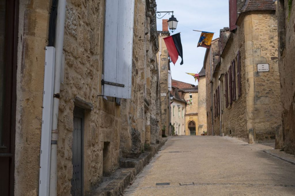 Une rue pavée étroite bordée de vieux bâtiments en pierre, de fenêtres aux volets et de drapeaux aériens dans une ville historique. Une rue pavée étroite bordée de vieux bâtiments en pierre, de fenêtres aux volets et de drapeaux aériens dans une ville historique.