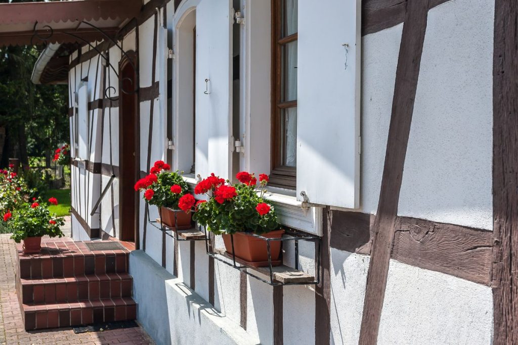 Une maison blanche à colombages avec des poutres brunes présente des fleurs rouges en pots sur les rebords des fenêtres. Il y a des marches en brique menant à l'entrée. Une maison blanche à colombages avec des poutres brunes présente des fleurs rouges en pots sur les rebords des fenêtres. Il y a des marches en brique menant à l'entrée.