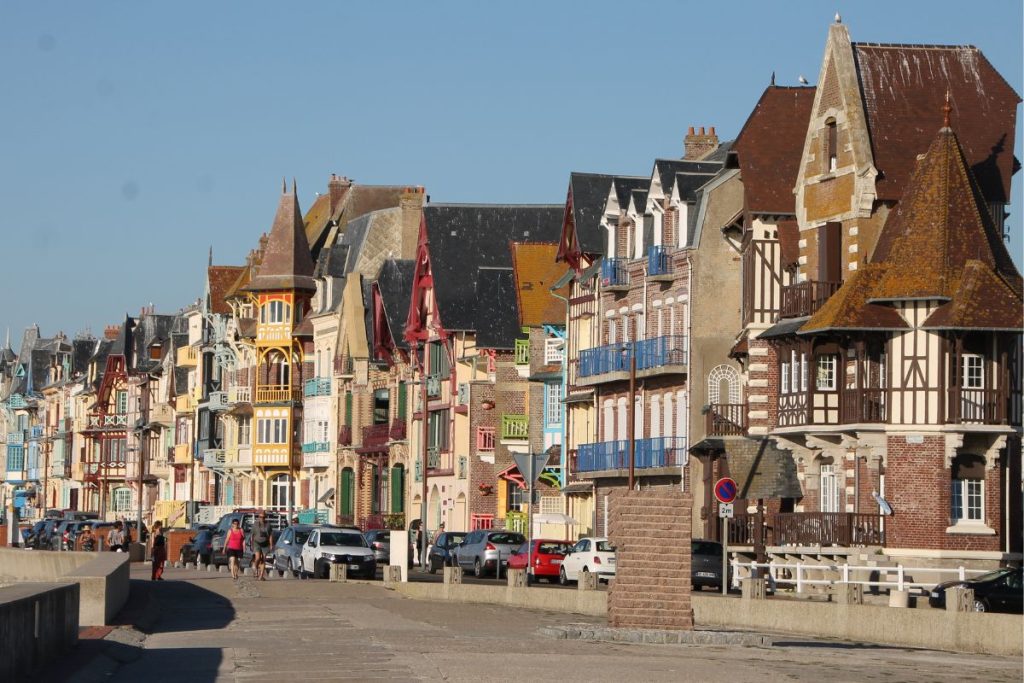 Des bâtiments colorés et richement ornés bordent une rue d'une ville côtière avec des voitures et des piétons garés. Des bâtiments colorés et richement ornés bordent une rue d'une ville côtière avec des voitures et des piétons garés.