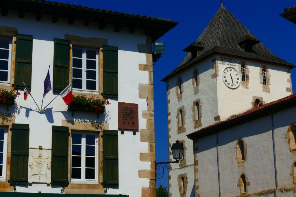 Par temps clair, un bâtiment aux volets et drapeaux verts jouxte une tour de l'horloge. L’horloge indique 10h55. Par temps clair, un bâtiment aux volets et drapeaux verts jouxte une tour de l'horloge. L’horloge indique 10h55.