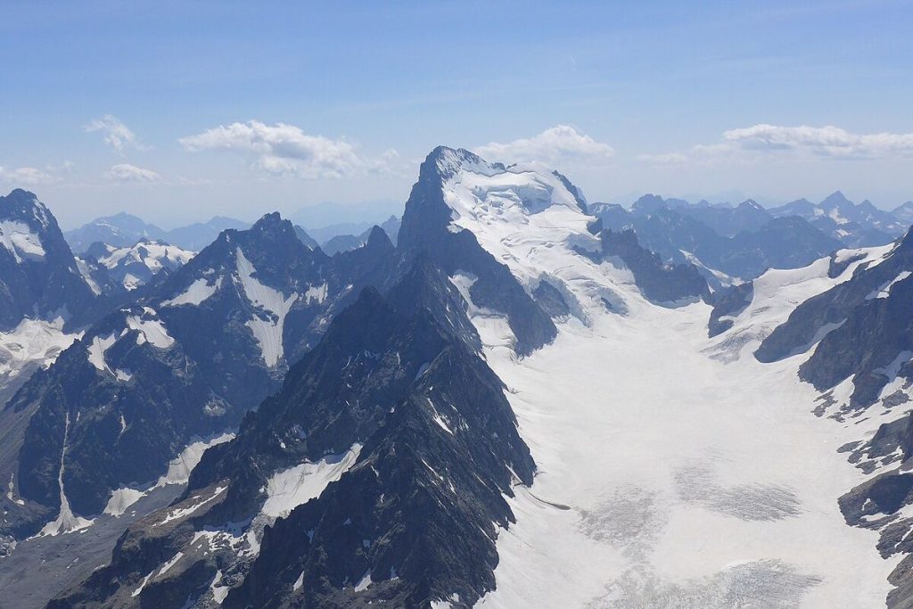 Des pics montagneux enneigés aux crêtes déchiquetées et un grand glacier sous un ciel bleu limpide.