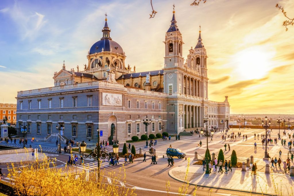 Cathédrale de l'Almudena à Madrid au coucher du soleil, avec des gens qui se promènent et se rassemblent sur la place environnante.