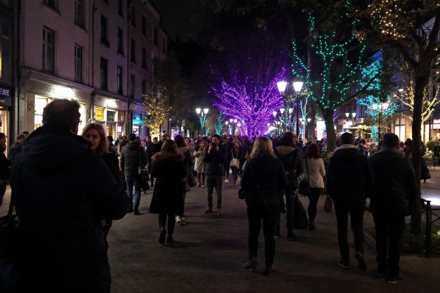 Rue nocturne bondée avec arbres décorés de lumières colorées