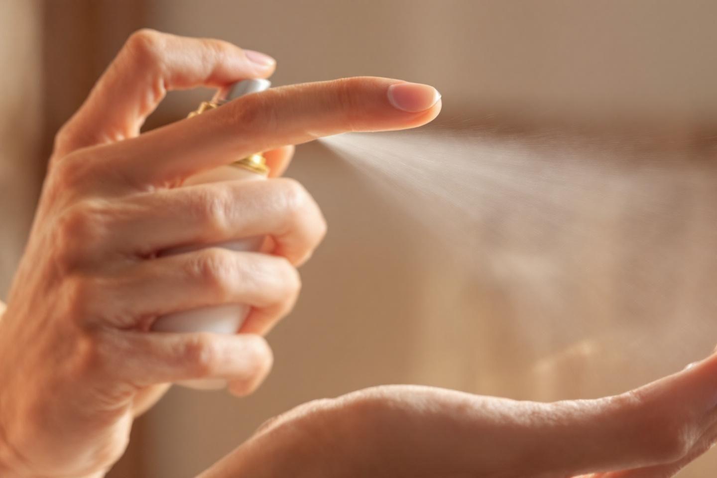 Main tenant un flacon de parfum en train de vaporiser