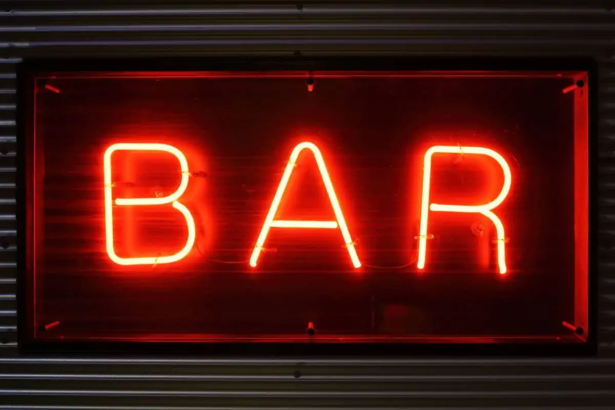 Une enseigne au néon rouge portant l'inscription « BAR », fixée sur un mur en tôle ondulée.