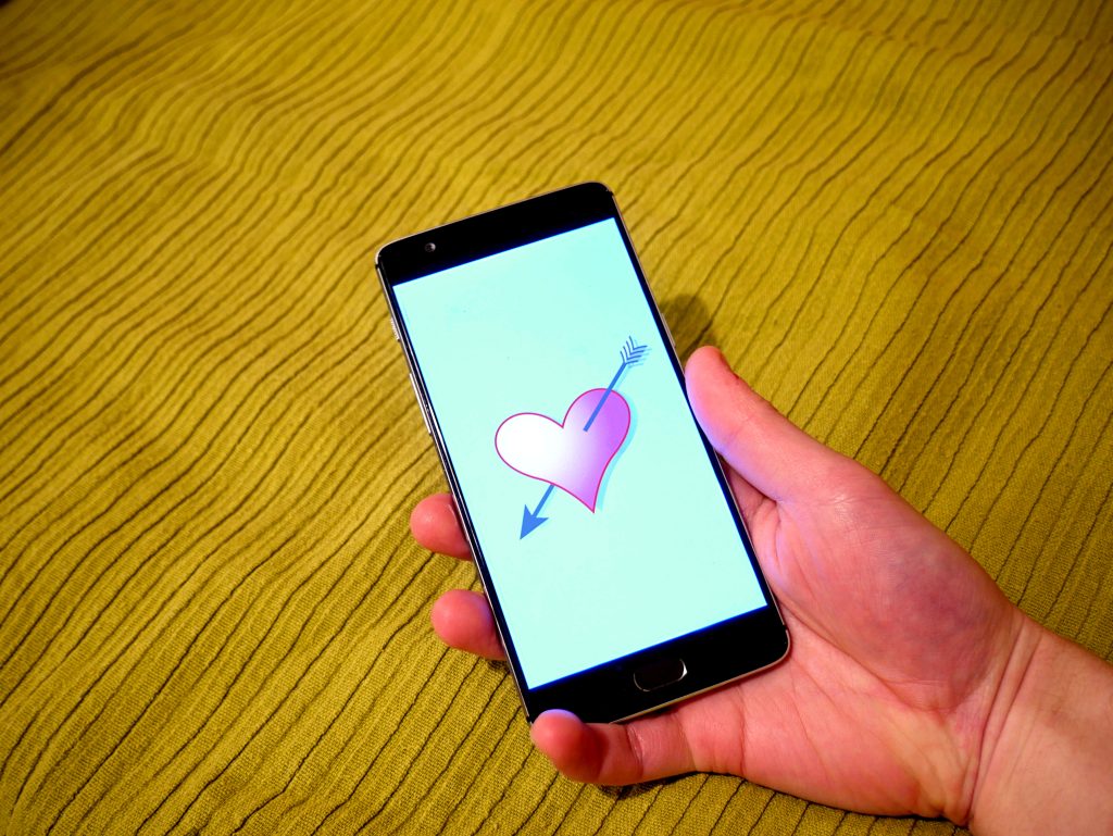 Main tenant un smartphone affichant un cœur transpercé d une flèche, symbole de message d amour